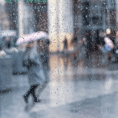 View of people with umbrellas through glass window with rain drops on glass 